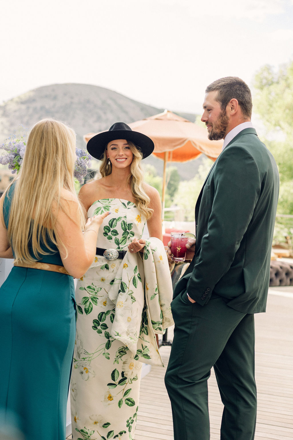 Bride in floral dress and groom in green suit enjoying welcome dinner conversation with guest during Jackson Hole wedding weekend